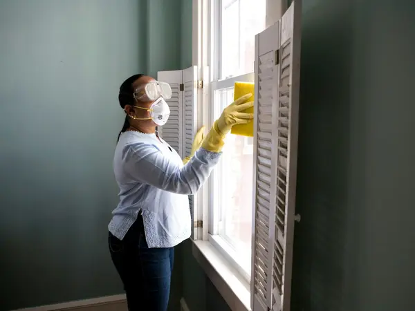A cleaner in gloves and a mask wiping a window, representing cleaning and facility services.